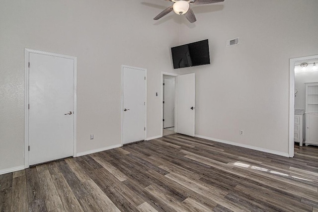 unfurnished bedroom featuring wood finished floors, a towering ceiling, visible vents, and baseboards