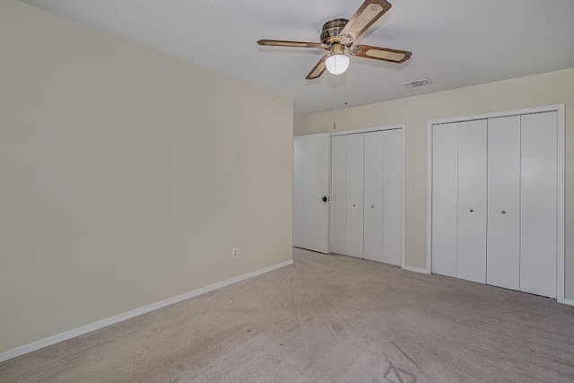 unfurnished bedroom with ceiling fan, visible vents, baseboards, carpet, and two closets