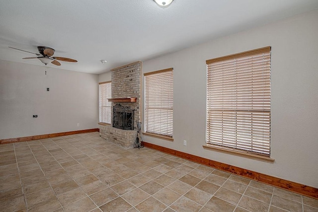 unfurnished living room featuring plenty of natural light, a brick fireplace, a ceiling fan, and baseboards