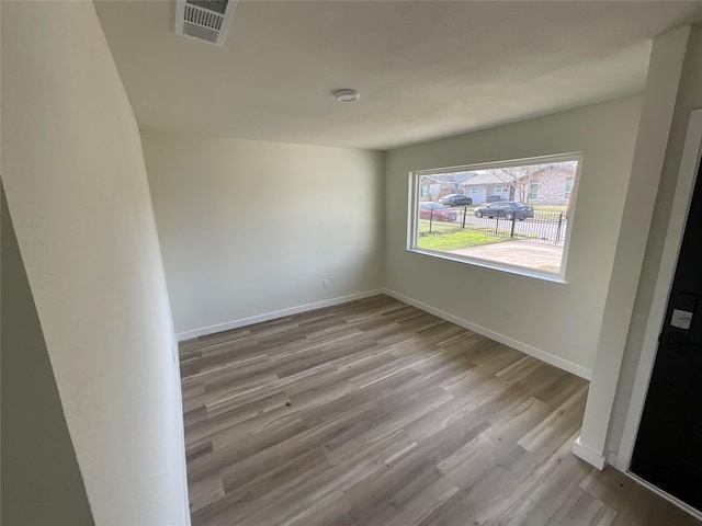 spare room featuring wood finished floors, visible vents, and baseboards