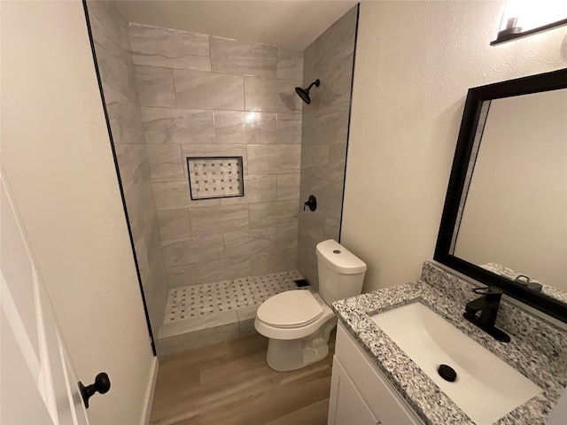 bathroom featuring a tile shower, vanity, toilet, and wood finished floors