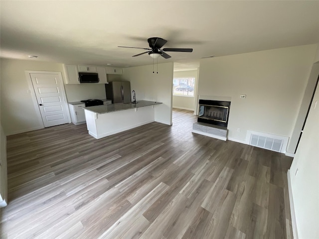 unfurnished living room featuring baseboards, visible vents, a glass covered fireplace, ceiling fan, and dark wood-type flooring