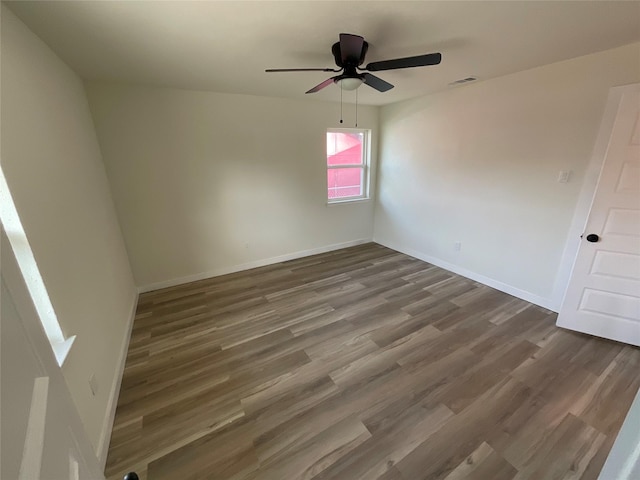 empty room featuring a ceiling fan, wood finished floors, visible vents, and baseboards