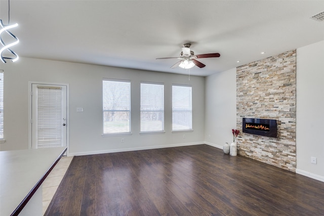 unfurnished living room with visible vents, a ceiling fan, wood finished floors, a stone fireplace, and baseboards