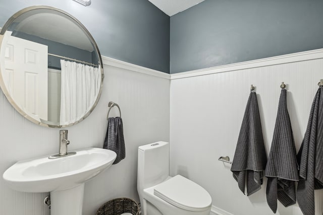 full bathroom featuring wainscoting, a sink, toilet, and a shower with curtain