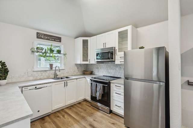 kitchen featuring stainless steel appliances, decorative backsplash, white cabinetry, vaulted ceiling, and a sink