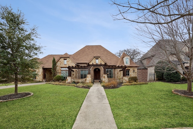 french country style house with stone siding, roof with shingles, and a front lawn