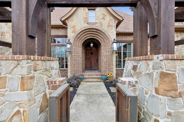 entrance to property with a shingled roof, stone siding, and brick siding