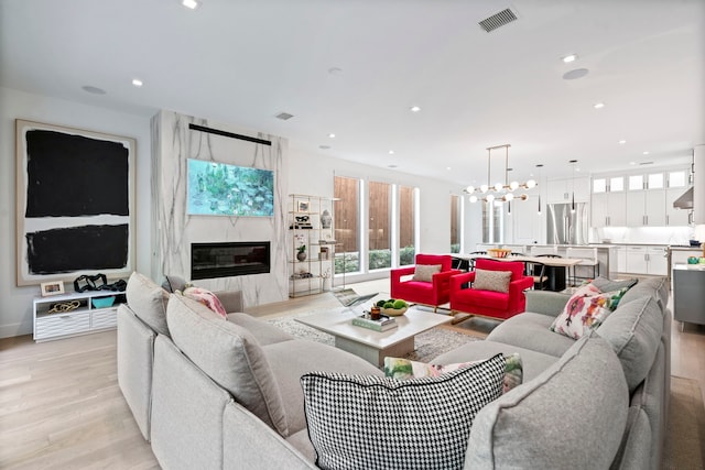 living room with light wood-style floors, a premium fireplace, visible vents, and a wealth of natural light