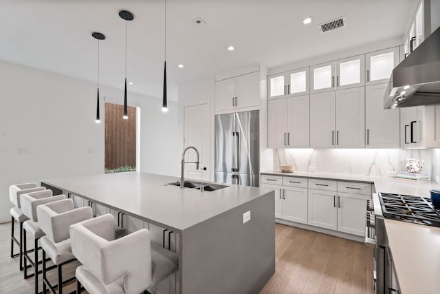 kitchen featuring visible vents, high quality fridge, a sink, an island with sink, and under cabinet range hood