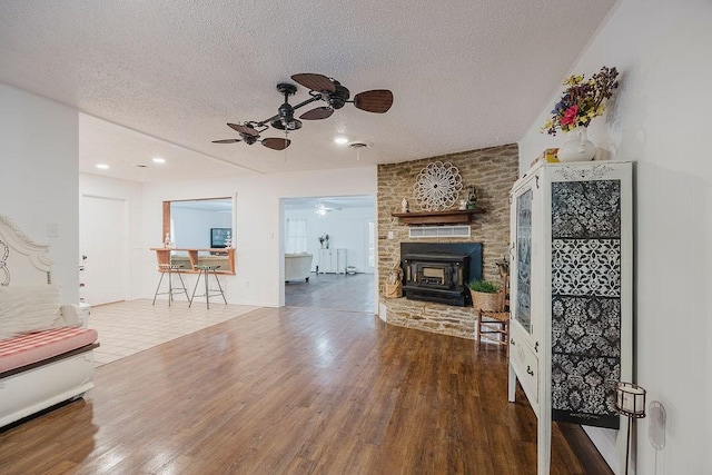 living room featuring a textured ceiling, a wood stove, a ceiling fan, and wood finished floors