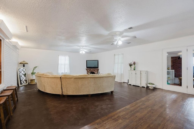 living room with visible vents, a ceiling fan, a textured ceiling, dark wood-style floors, and a fireplace