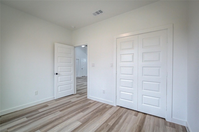 unfurnished bedroom featuring light wood-style floors, baseboards, visible vents, and a closet