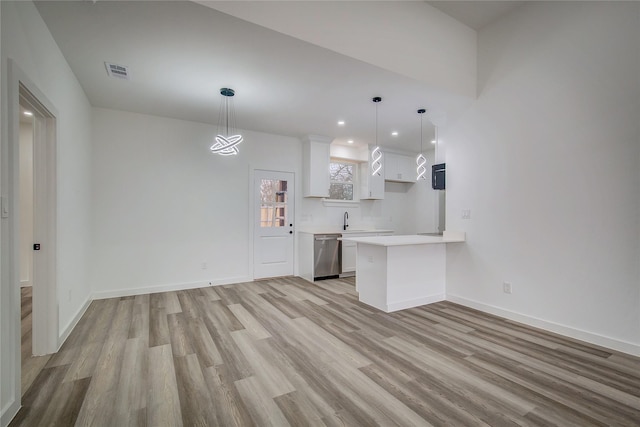 kitchen featuring light wood finished floors, white cabinets, dishwasher, a peninsula, and light countertops