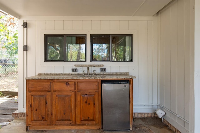 bar with indoor wet bar, wood walls, freestanding refrigerator, and a sink