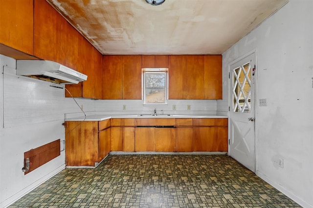 kitchen featuring brown cabinets, under cabinet range hood, light countertops, and a sink