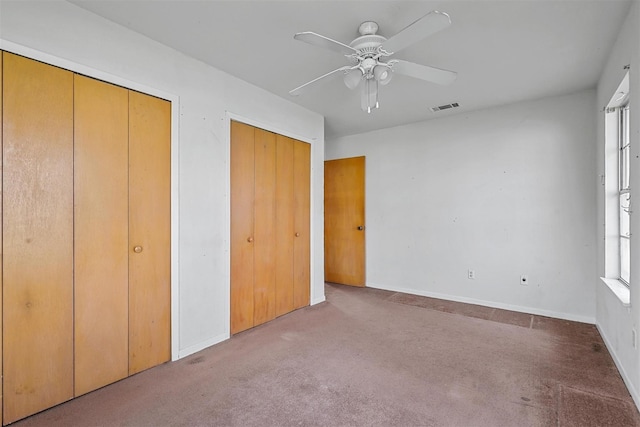 unfurnished bedroom featuring carpet floors, two closets, visible vents, and baseboards