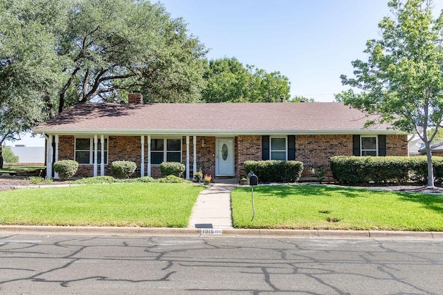 ranch-style home with brick siding, a chimney, a front lawn, and roof with shingles