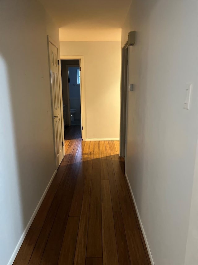 hall with dark wood-style flooring and baseboards