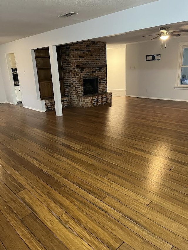 unfurnished living room with a fireplace, visible vents, hardwood / wood-style floors, ceiling fan, and baseboards