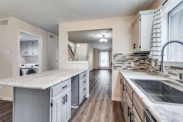 kitchen featuring a sink, visible vents, decorative backsplash, dark wood-style floors, and washer and clothes dryer