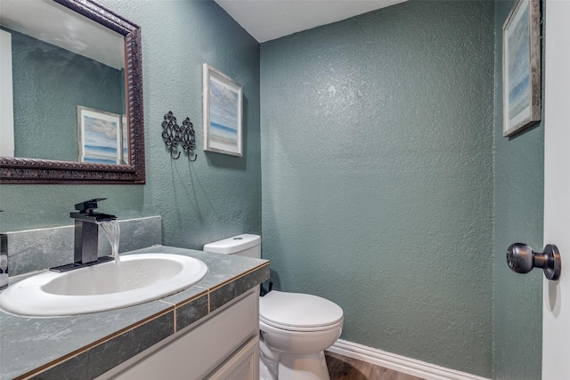 bathroom with a textured wall, vanity, toilet, and wood finished floors