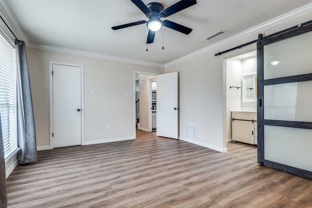 unfurnished bedroom with a barn door, visible vents, light wood-style flooring, and ornamental molding