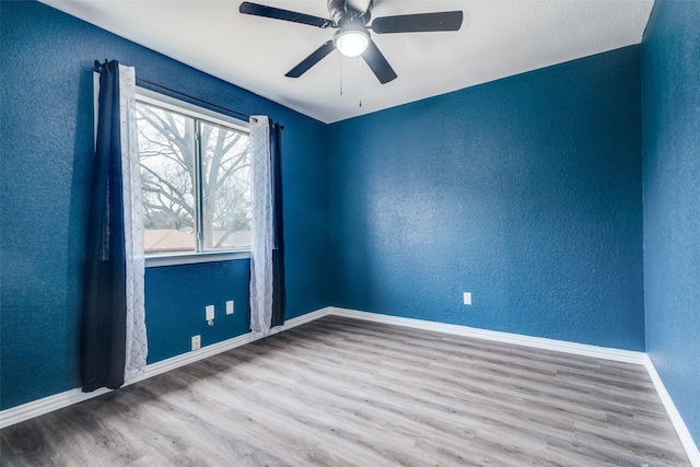 unfurnished room with a ceiling fan, baseboards, wood finished floors, and a textured wall