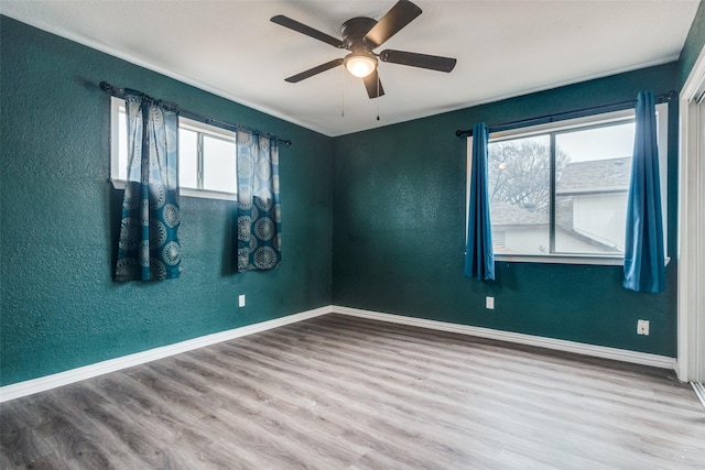 empty room featuring a ceiling fan, a textured wall, baseboards, and wood finished floors