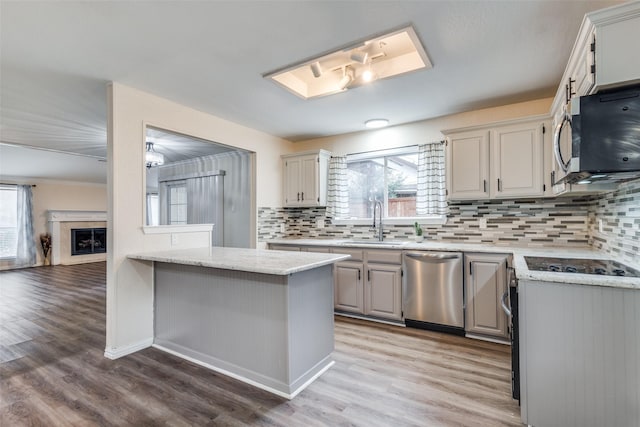 kitchen featuring light wood finished floors, tasteful backsplash, appliances with stainless steel finishes, a fireplace, and a sink