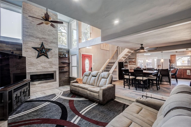 living area featuring stairs, a fireplace, ceiling fan, and wood finished floors