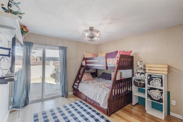 bedroom featuring access to exterior, baseboards, a chandelier, and wood finished floors