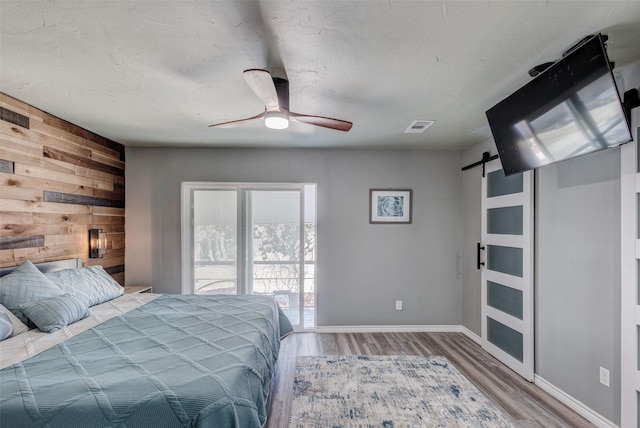 bedroom with a barn door, wood finished floors, visible vents, and wooden walls