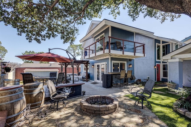 rear view of property with a fire pit, a patio, a balcony, and stucco siding