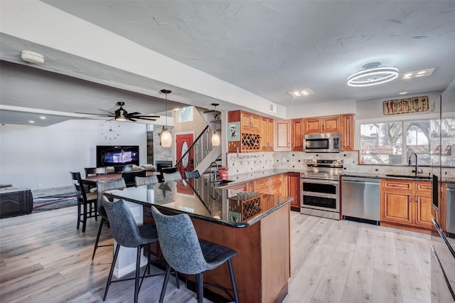 kitchen featuring light wood finished floors, stainless steel appliances, backsplash, a sink, and dark stone counters