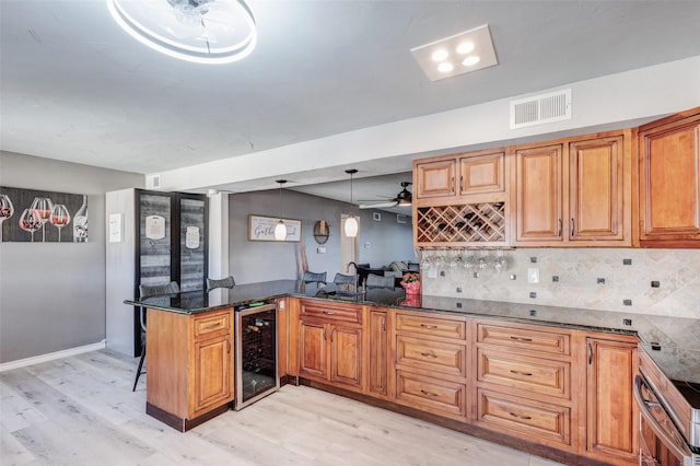 kitchen with visible vents, brown cabinetry, dark stone counters, beverage cooler, and a peninsula