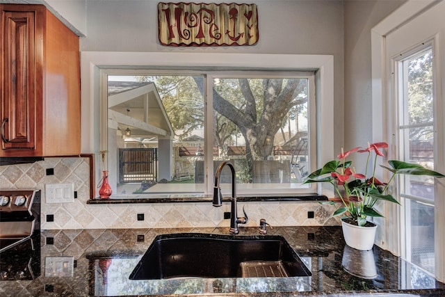 kitchen with electric range, a sink, backsplash, dark stone counters, and brown cabinetry