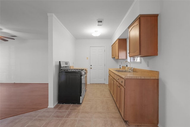 kitchen with ceiling fan, light tile patterned floors, a sink, range with gas stovetop, and crown molding