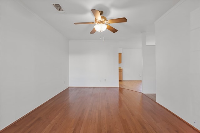 spare room featuring ornamental molding, light wood-type flooring, visible vents, and a ceiling fan