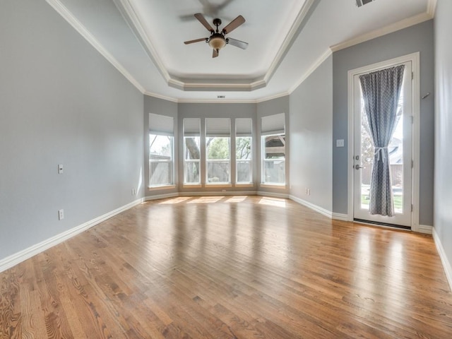 unfurnished room featuring a raised ceiling, ornamental molding, wood finished floors, and baseboards