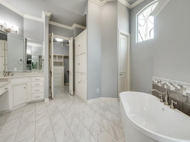 full bathroom with marble finish floor, a soaking tub, a spacious closet, ornamental molding, and vanity