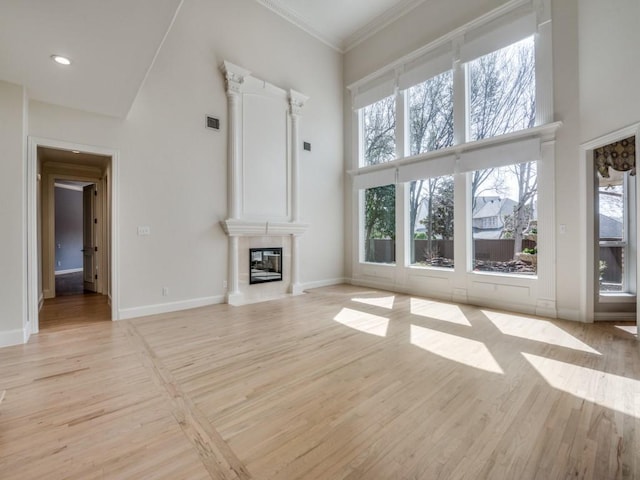 unfurnished living room with light wood-type flooring, a high ceiling, a tiled fireplace, and baseboards