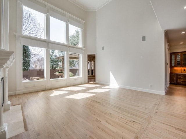 unfurnished living room featuring ornamental molding, baseboards, light wood-style flooring, and a high ceiling