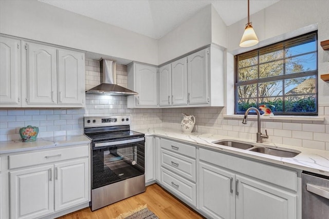 kitchen with stainless steel appliances, a sink, white cabinetry, wall chimney range hood, and light wood finished floors