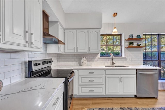 kitchen with a sink, white cabinets, wall chimney range hood, appliances with stainless steel finishes, and light wood-type flooring