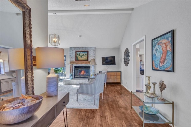 living area featuring lofted ceiling with beams, a brick fireplace, a textured ceiling, wood finished floors, and baseboards