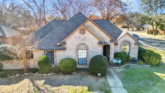 view of front of house featuring brick siding and roof with shingles