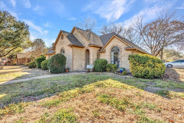 view of front of property with a shingled roof, a front yard, and brick siding