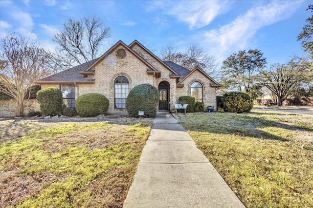 french country inspired facade with a shingled roof, a front yard, and brick siding