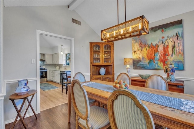 dining space featuring lofted ceiling with beams, wood finished floors, visible vents, and a chandelier